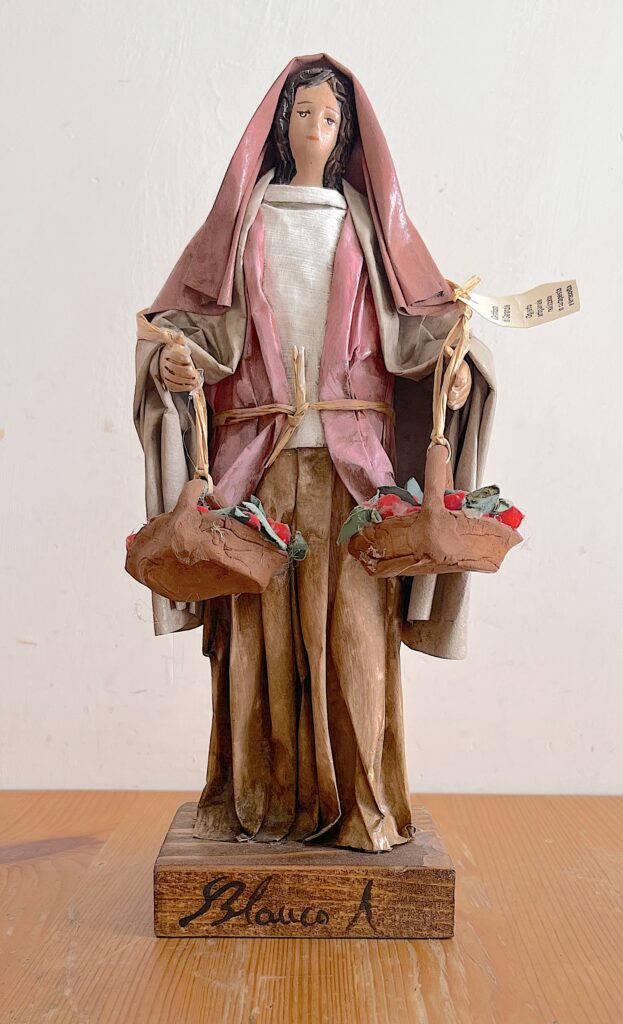 Statuina vintage in cartapesta leccese raffigurante una venditrice di frutta con due cesti, veste rosa e beige e base in legno firmata.
